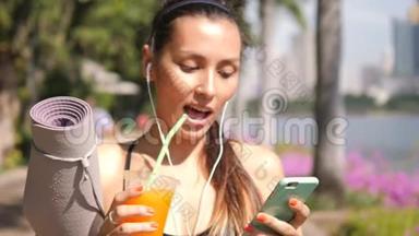 城市公园晨练瑜伽后，年轻混合种族运动员使用智能手机和饮用新<strong>鲜橙</strong>汁